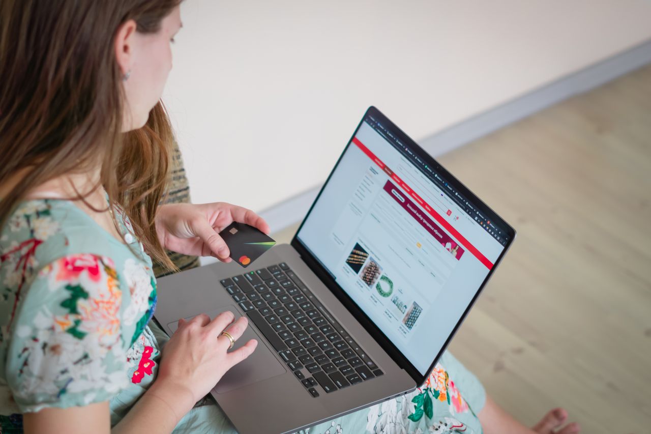 Woman in floral dress shopping online with a laptop and credit card indoors.